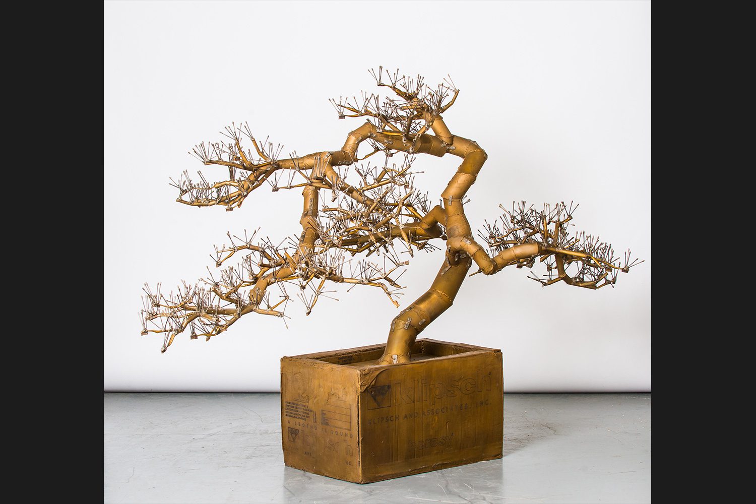 Bonsai originated as part of an immersive sculptural installation, Tea Ceremony, at The Noguchi Museum in 2016. Characteristic of Sachs, the tree plays with the concepts of luxury and utility, and reveals its raw construction and process. Branches made of cue-tips and toothbrush handles join a carboard trunk, the whole consisting of over 3,000 individual pieces. Sachs revels in materiality and imperfections. Exposed hinges bring attention to the naked weld joints as the thin layer of cast bronze seems to highlight the original markings of the reused carboard.Download this study guide.